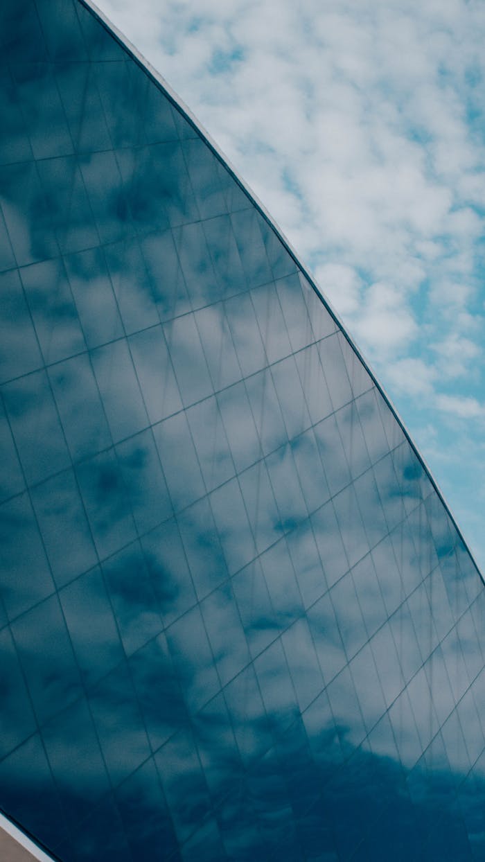Abstract view of a modern glass facade reflecting a blue sky with clouds, showcasing urban architecture.