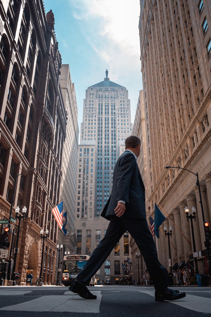 Businessman in suit crossing street in downtown Chicago with skyscrapers and flags.